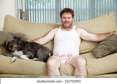 Discouraged Unemployed Man At Home In His Underwear, Sitting On The Couch With His Dog.  