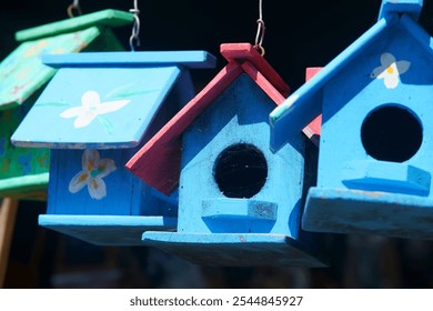 Discover a charming trio of colorful wooden birdhouses hanging in a sunny outdoor setting, ideal for adding whimsy to gardens and inviting local wildlife. - Powered by Shutterstock