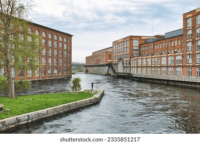 Discover Tampella's charm, old brick factory area in Tampere, Finland, alongside Vapriikki museum. Green island with a statue in the foreground, Tammerkoski river flows through