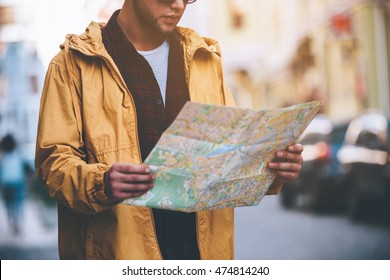 Discovering New Places. Close-up Of Handsome Young Man Holding Map And Looking At It While Standing On The City Street