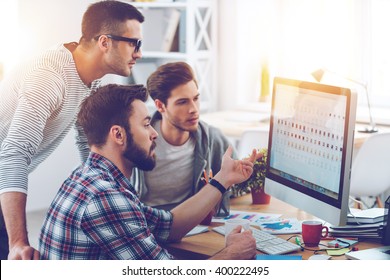 Discussing New Project. Three Young Business People Discussing Something While Looking At The Computer Monitor Together 