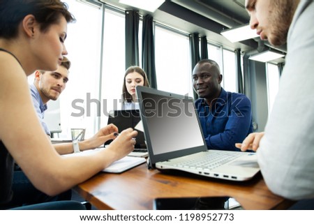 Discussing successful project. Group of young cheerful business people working and communicating while sitting at the office desk together with colleagues sitting in the background