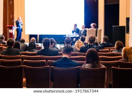 Discussions and Round Table Concepts. Host Speaking In Front of the White Screen on Stage for the Group of Business People at a  Conference. Horizontal Image