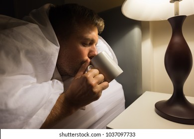 Diseased Caucasian Mature Man Drink The Water On The Bed Closeup At Night. He Has Hangover After Party Or Flu