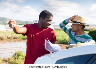 Disgruntled African American Farmer Holding Papers, Reprimanding Hispanic Contractor For Poor Job Outdoors