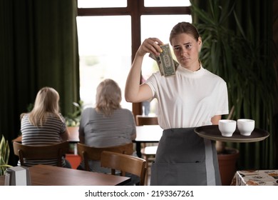 Disgruntled Female Waiter Holding Serving Tray In Restaurant With Bad Tips, Copy Space