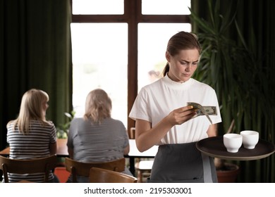 Disgruntled Female Waiter Holding Serving Tray In Restaurant With Bad Tips, Copy Space