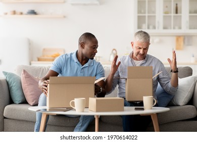 Disgruntled online shopper. Broken item, delivery problem, spoiled defective goods. Confused shocked millennial african american and old caucasian men opening boxes with wrong product in living room - Shutterstock ID 1970614022