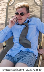 Disgruntled Young Businessman Downshifter Talks On The Phone Lying On A Sun Lounger On The Beach In A Shirt, Tie And Boxer Shorts. Vertical Shot