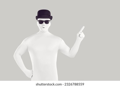 Disguised man dressed in white bodysuit pointing to side with forefinger. Portrait of faceless man wearing full body spandex costume, black bowler hat and sunglasses pointing finger to copy space - Powered by Shutterstock