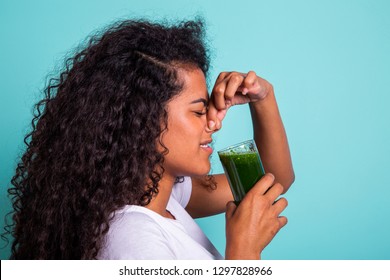 Disgusted Africanwoman Tasting A Vegetable Juice With Bad Flavor On Green Background