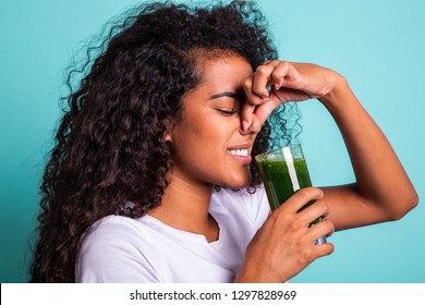 Disgusted Africanwoman Tasting A Vegetable Juice With Bad Flavor On Green Background