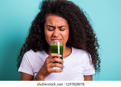 Disgusted Africanwoman Tasting A Vegetable Juice With Bad Flavor On Green Background