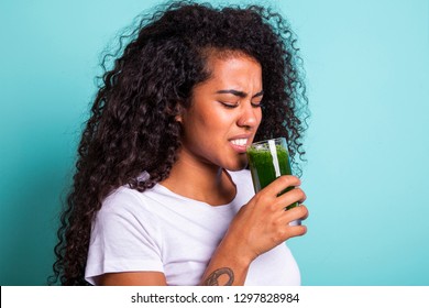 Disgusted Africanwoman Tasting A Vegetable Juice With Bad Flavor On Green Background