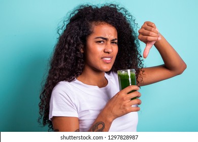 Disgusted Africanwoman Tasting A Vegetable Juice With Bad Flavor On Green Background