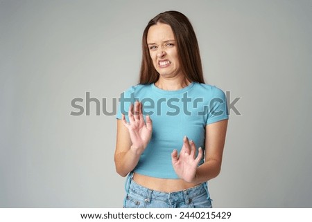 Disgusted and frowning young woman on gray background