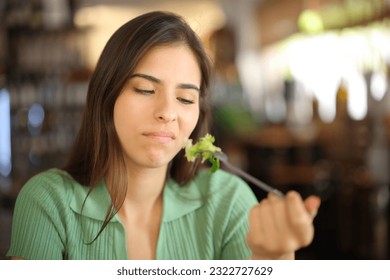 Disgusted woman eating lettuce sitting in a restaurant