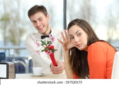 Disgusted woman rejecting a geek boy offering flowers in a blind date in a coffee shop interior