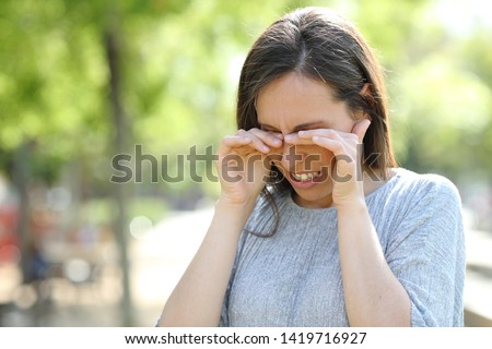 Disgusted woman rubbing her eyes standing outdoors in a park