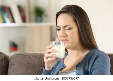 Disgusted Woman Tasing Milk With Bad Flavor Sitting On A Couch In The Living Room At Home