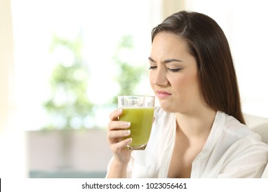 Disgusted Woman Tasting A Vegetable Juice With Bad Flavor Sitting On A Couch In The Living Room At Home