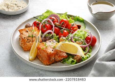 Dish with baked Salmon steak fillet with fresh green salad with vegetables, tomatoes, onion, lemon in a plate. Keto diet concept healthy food, close up.
