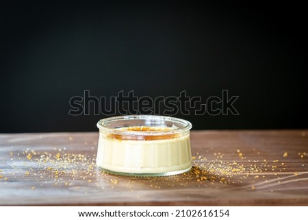 Dish of Creme Brûlée french dessert sprinkled with sugar in a glass bowl on a wood surface