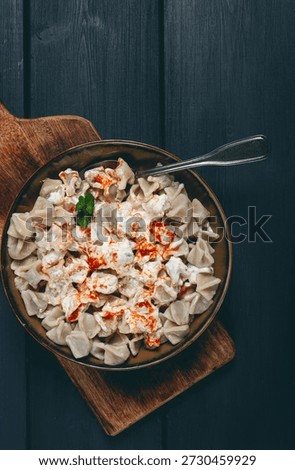 The dish features a generous serving of Turkish dumplings topped with velvety yogurt and a drizzle of spicy red sauce, .