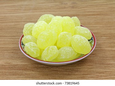 A Dish Filled With Lemon Drops On A Wood Surface.