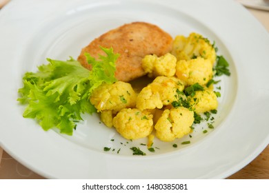 A Dish Of Fried Chicken Cutlet And Boiled Cauliflower In A Plate In The Interior Of The Restaurant.