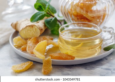 Dish of ginger tea, ginger root and slices of candied ginger on a white kitchen table selective focus.
