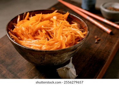 Dish of Korean and Asian cuisine: vegetable salad marinated carrots with garlic. Served in ceramic bowl with chopsticks. Seasoning in small bowls on Mocha Mousse tones table. Healthy eating. Close-up - Powered by Shutterstock