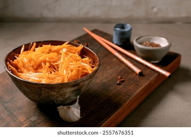 Dish of Korean and Asian cuisine: vegetable salad marinated carrots with garlic. Served in ceramic bowl with chopsticks. Seasoning in small bowls on Mocha Mousse tones table. Healthy eating. Close-up - Powered by Shutterstock