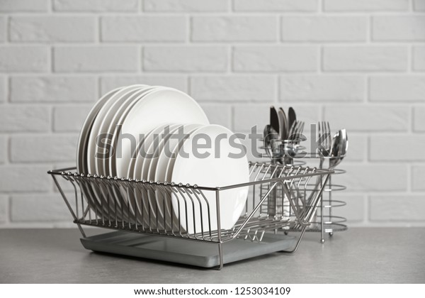 Dish rack\
with clean plates on table near brick\
wall