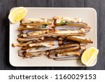 dish of razor clam grilled with garlic, parsley, olive oil and lemon slice on wood table