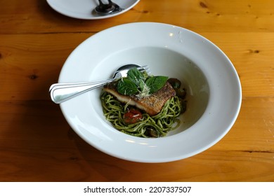 A dish of spaghetti pesto with grilled sea bass fillet on the wooden table. - Shutterstock ID 2207337507