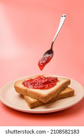 un plato de tostadas esparcidas con mermelada y una cuchara de levitación sobre un fondo rosa pastel.