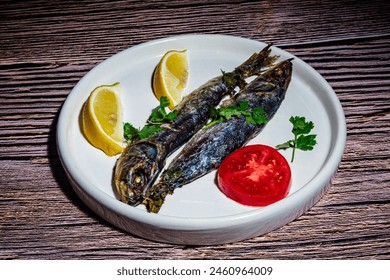 A dish with two oven-roasted sardines, accompanied with lemon, parsley and tomato. - Powered by Shutterstock