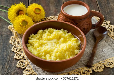 Dish Of Useful Grains - Millet Porridge In A Clay Bowl, Milk In A Cup, A Wooden Spoon On A Linen Napkin And A Wooden Table. Selective Focus