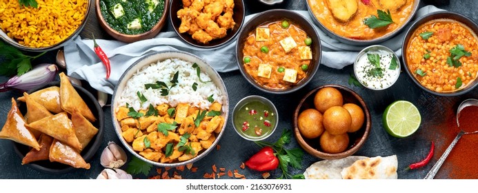 Dishes of indian cuisine. Curry, butter chicken, rice, lentils, paneer, samosa, spices. Bowls and plates with indian foodon dark on dark background. Top view, panorama.