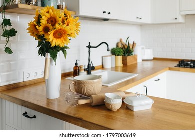 Geschirr und Geschirr auf dem Küchentisch, kochenfertig. weiße, moderne Küche im skandinavischen Stil, Küchendetails, Holztisch, Blumenstrauß auf Vase auf dem Tisch