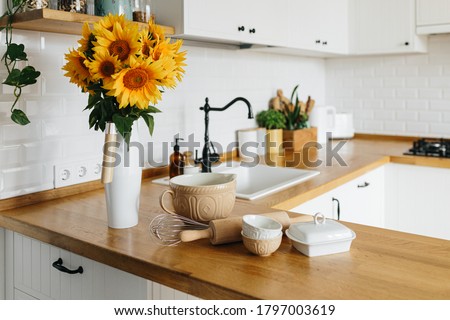 Dishes and utensils on kitchen table, ready to cook. white simple modern kitchen in scandinavian style, kitchen details, wooden table, sunflowers bouquet in vase on the table