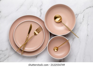 Dishes and utensils for serving and eating meals. Beige round rimmed plates and gold colored cutlery on a white marble table, top view. Modern ceramic crockery, trendy tableware - Shutterstock ID 2122554749