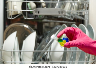 Dishwasher Detergents in hands. hands in pink golvs holds dishwasher gel capsules. Capsule for the dishwasher. Brilliant cleanliness.