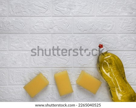 Dishwashing tools. Tips for quick house cleaning. Copy space. Template for advert, article. Three yellow sponges for cleaning and bottle of household chemicals on brick wall. Space for text. Flat lay