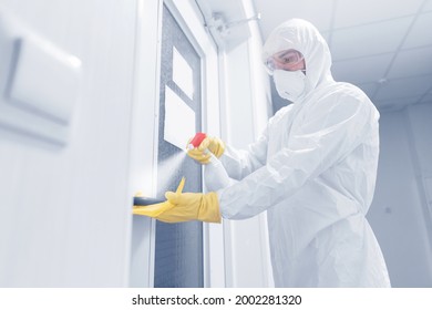 Disinfect Employee In Medical Suit Cleans Hotel Apartment Lobby From Virus And Bacteria. Man Holding Antiseptic Spray Against Coronavirus.