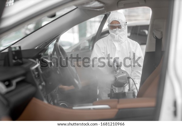 Disinfectant worker character in
protective mask and suit sprays bacterial or virus in a
car.