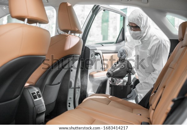 Disinfectant worker character in\
protective mask and suit sprays bacteria or virus in a\
car.