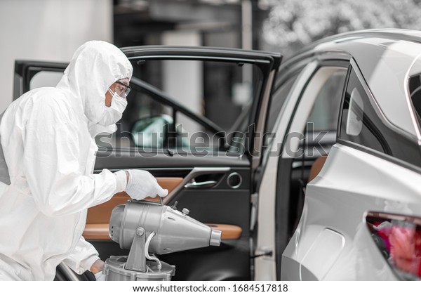 Disinfectant worker character in\
protective mask and suit sprays bacterial or virus in a\
car.