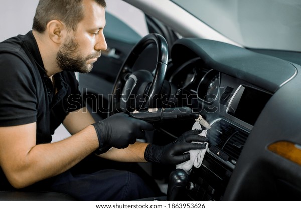 Disinfecting\
the car interior, steam heat disinfection of vehicles. Close up of\
young bearded man worker, cleaning car air conditioner and control\
panel with high pressure hot steam\
cleaner